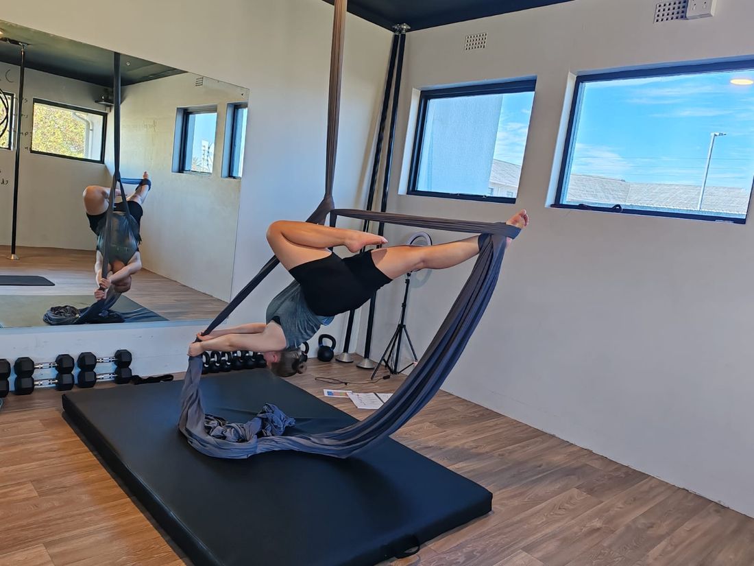 Aerial silks inversion beside the studio's dumbbell and kettlebell rack