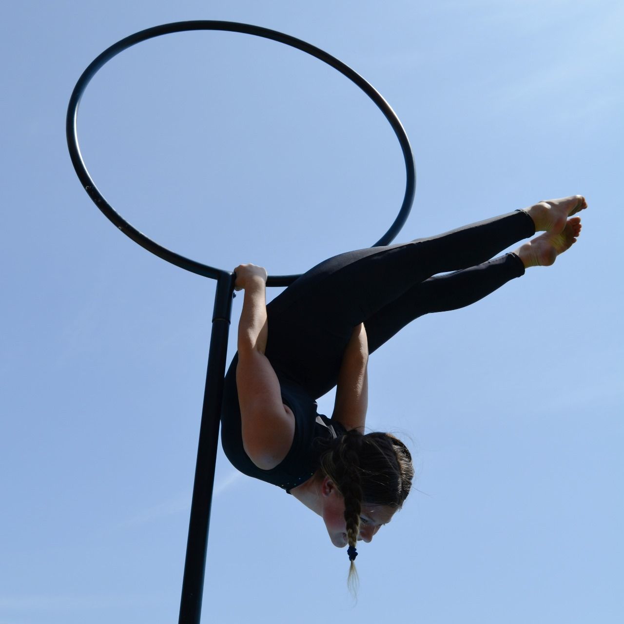Aerial hoop artist inverted in a lyra against a clear blue sky